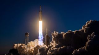 a white spacex falcon heavy rocket launches into a dark evening sky